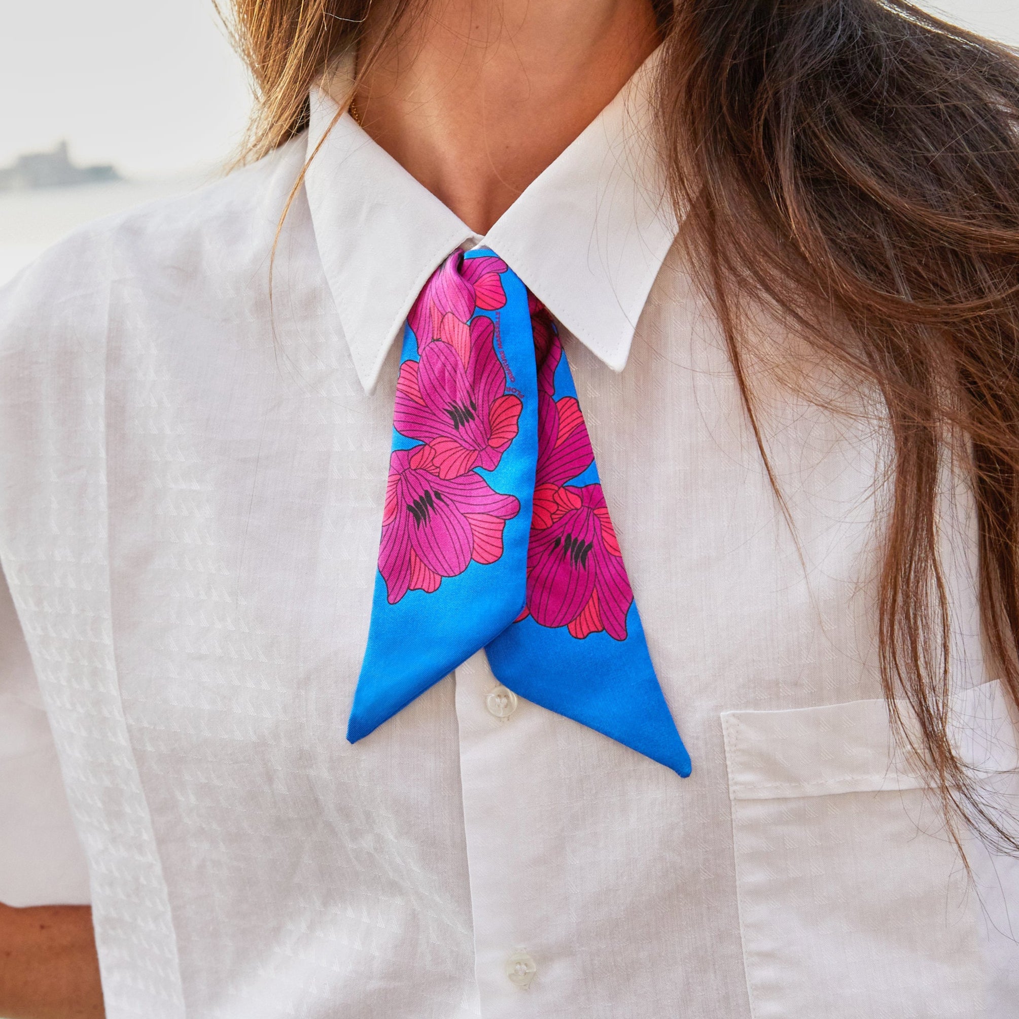 silk twilly flor bleu with pink flowers tied around a womans neck wearing a white shirt 