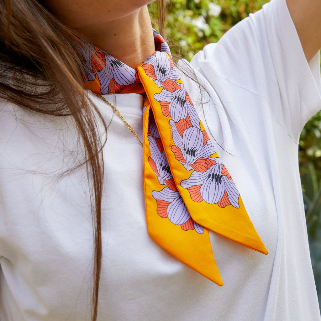 silk twilly flor jaune soleil with purple and orange flowers tied around a womans neck wearing a white tshirt